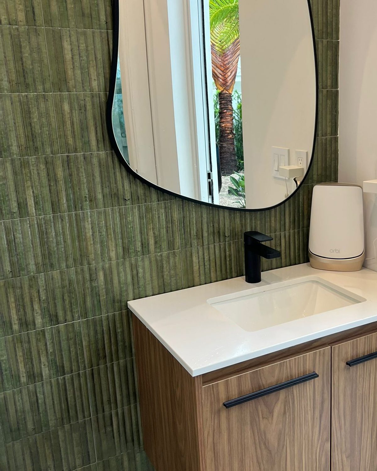 Green textured tile bathroom with walnut floating vanity and organic mirror