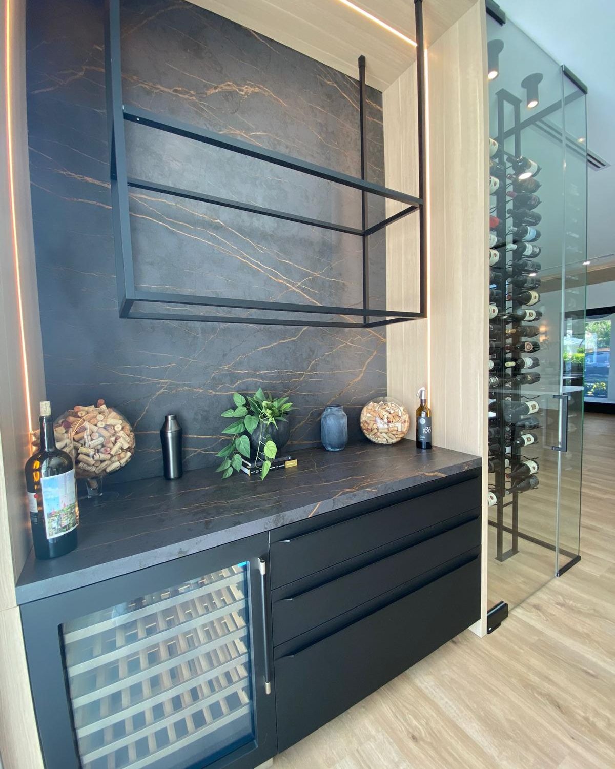 Custom dry bar with dark veined marble back wall, black metal shelving and adjoining wine room