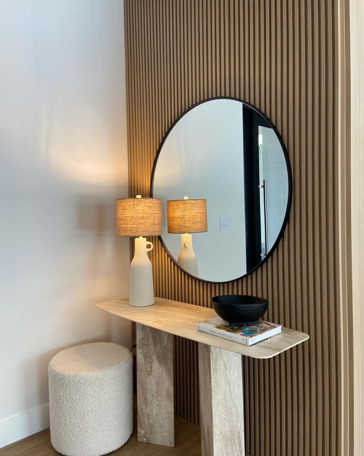 Entry vignette with travertine console, round mirror and slatted wood wall