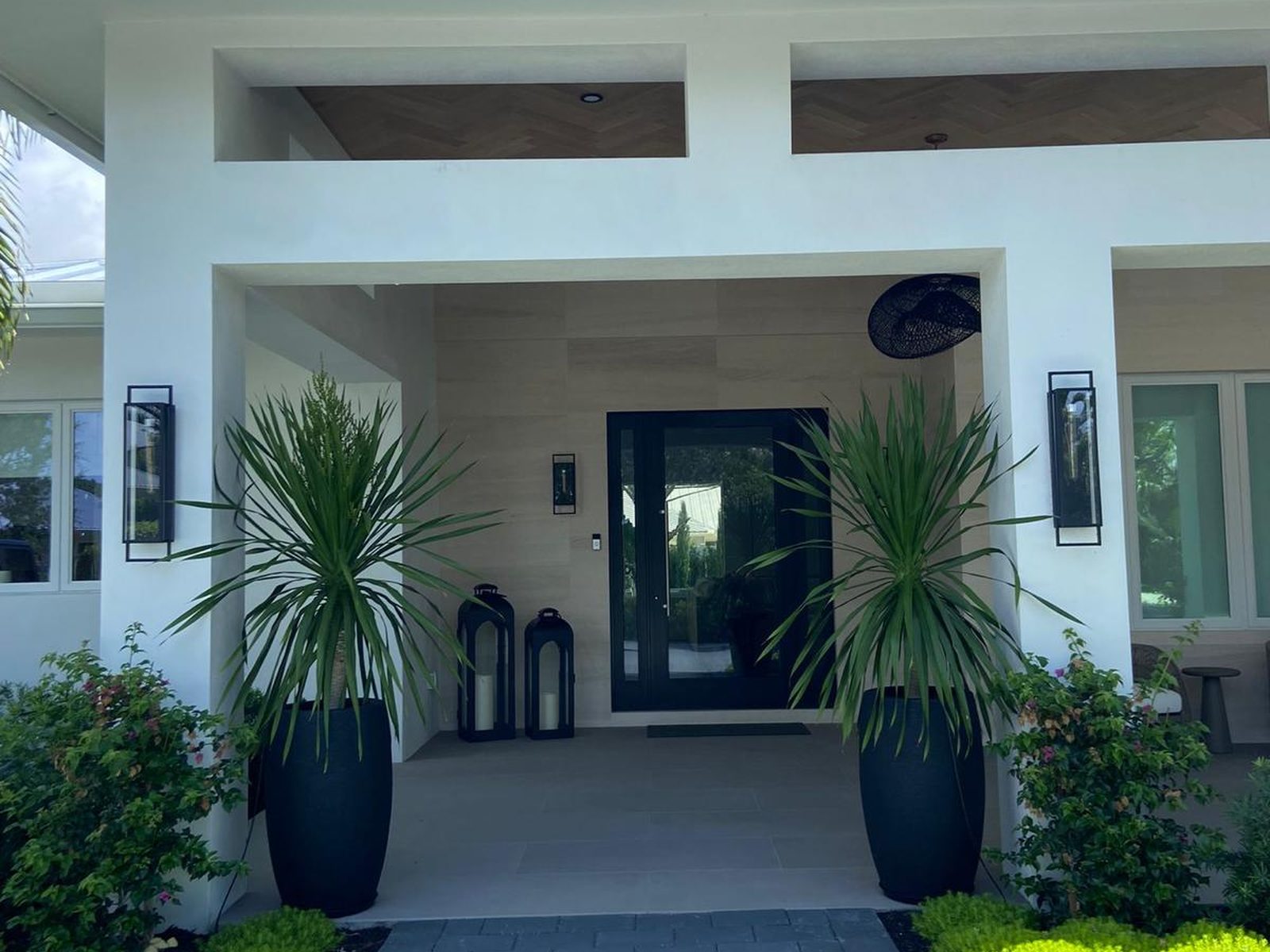 Roth Romano residence entry — modern Delray Beach home with wood-paneled ceiling, twin palms, and black-framed glass doors