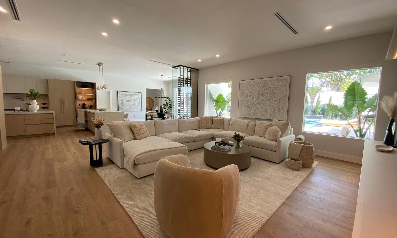 Open-plan living and kitchen in a Delray Beach whole-home renovation by Acassa Construction — wide-angle view with sectional sofa, wine room, dining area and pool visible through windows