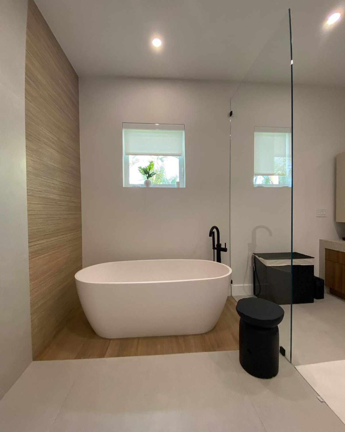 Freestanding soaking tub in a primary bath, with wood-paneled accent wall and matte black fixtures