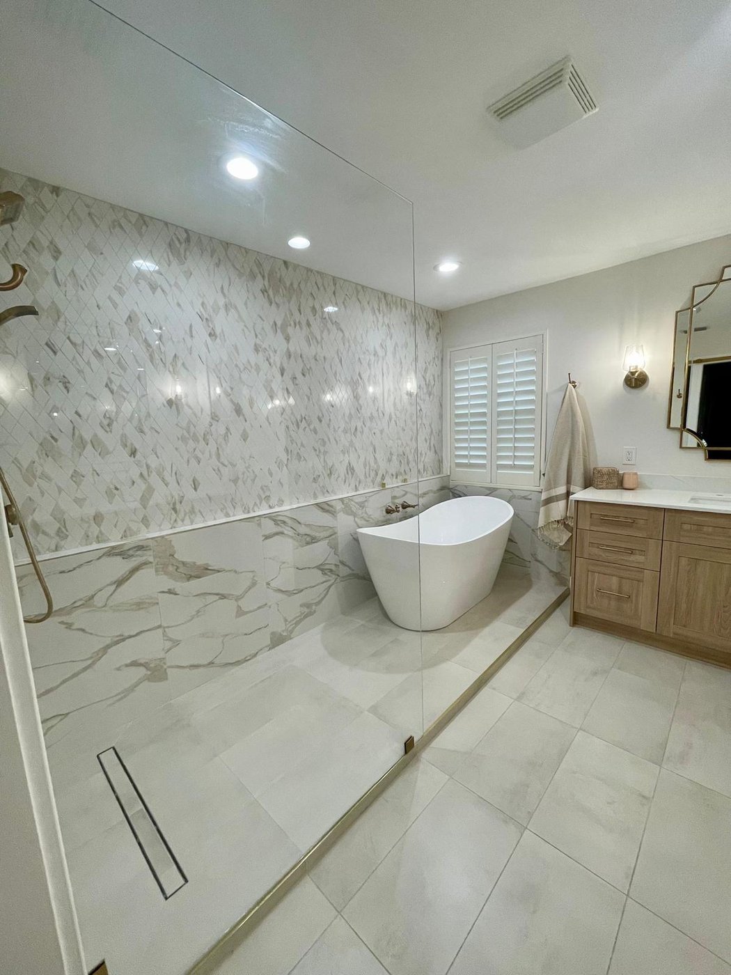 Renovated primary bath with marble walls, freestanding tub, and walk-in shower in the Bashiri residence