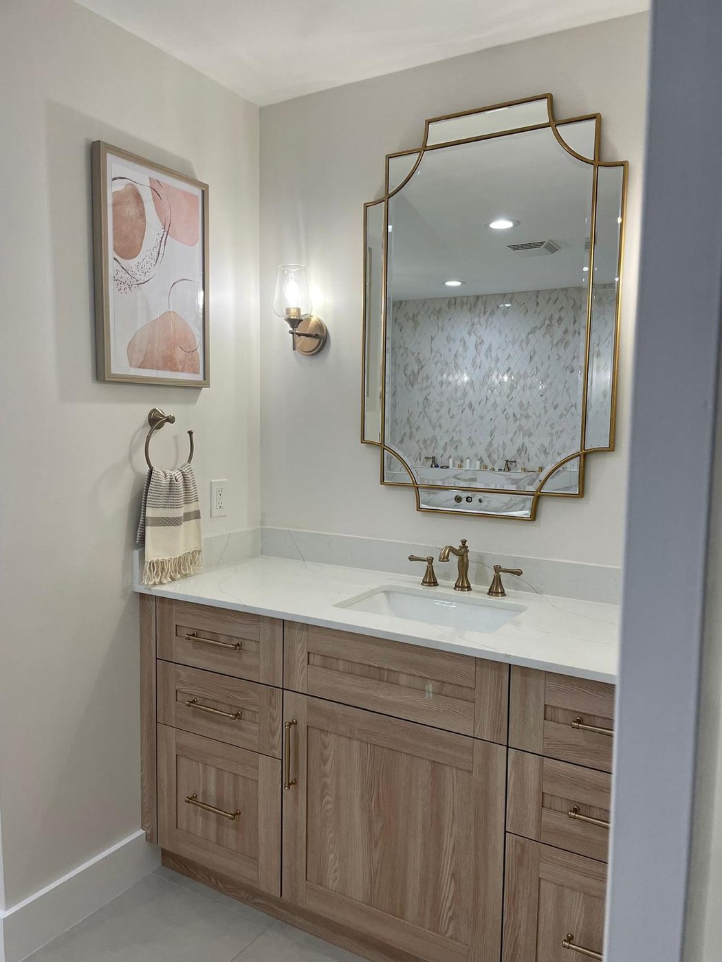 Renovated primary bath vanity with framed mirror and warm-tone oak cabinetry