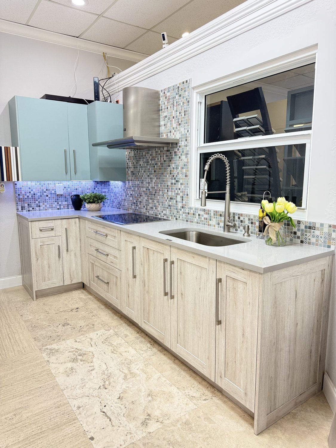 Showroom kitchen vignette with sage-green cabinetry, light wood accents, and brushed gold hardware
