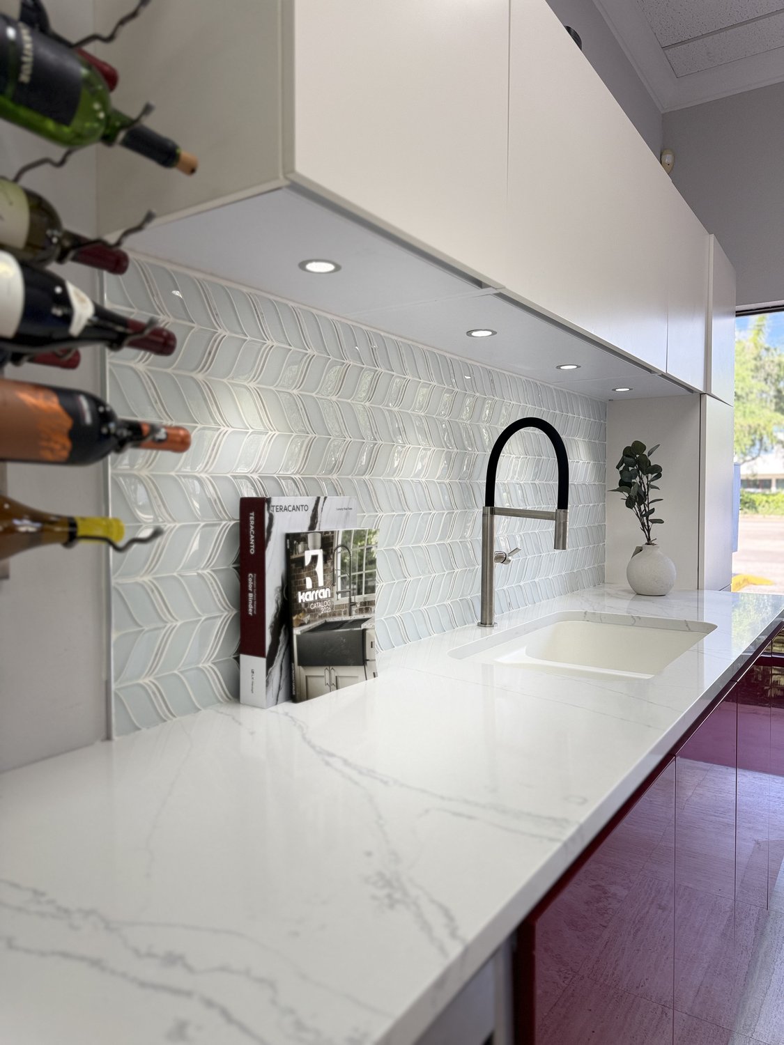 Showroom vignette of a white cabinetry run with a wine display, brushed-brass faucet, and a long stone counter