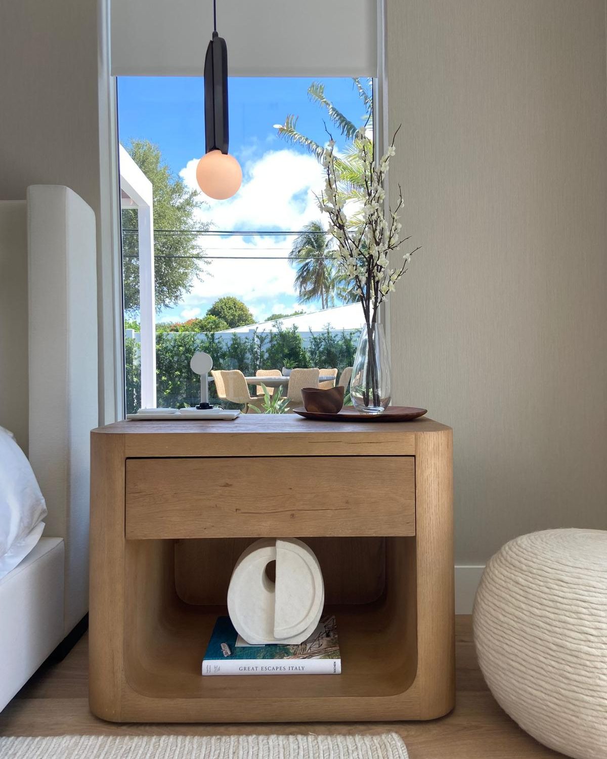 A finished bedroom vignette with sculpted oak nightstand, modern pendant, and styled accents, the kind of finish details specified at the Acassa studio